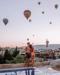 a man and woman standing next to a swimming pool with hot air balloons at Cappadocia Caves Hotel in Goreme