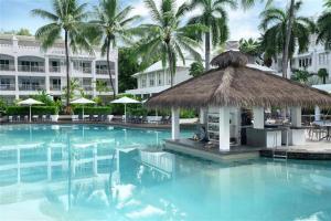 a large swimming pool with a straw hut in front of a hotel at Beach Club Palm Cove 2 Bedroom Luxury Penthouse in Palm Cove