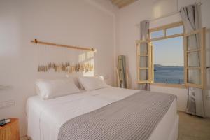a white bedroom with a large bed and a window at Faro Sunset Suites in Mikonos