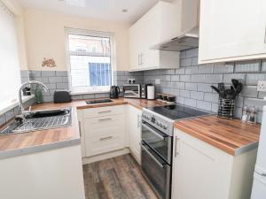 una cocina con armarios blancos y electrodomésticos de acero inoxidable en Sandy Toes Cottage en Newbiggin-by-the-Sea