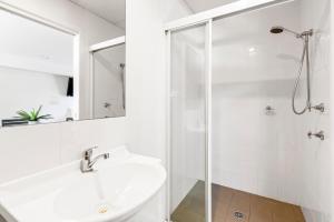 a white bathroom with a shower and a sink at Surf Beach Motel Coffs in Coffs Harbour