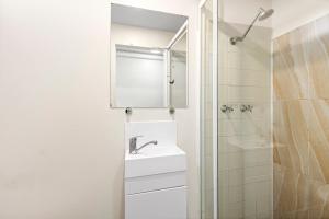 a white bathroom with a sink and a shower at Surf Beach Motel Coffs in Coffs Harbour