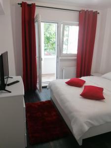 a bedroom with two beds with red curtains and a window at Apartament Racadau in Braşov