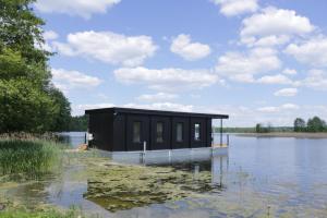 un pequeño edificio negro sentado sobre un cuerpo de agua en Dom na Wodzie, en Kruklanki