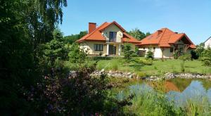 une maison avec un toit rouge à côté d'un étang dans l'établissement Apartamenty Zaczarowany Ogród, à Kazimierz Dolny