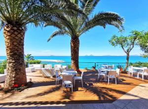 un restaurante con palmeras, mesas y el océano en Villa Anita Apartments, en Capo dʼOrlando