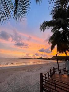 a sunset on a beach with a bench and a palm tree at Casa Maragogi in Maragogi
