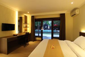 een slaapkamer met een bed, een bureau en een televisie bij Hotel Melamun in Lovina
