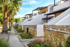 a building with a stone wall and palm trees at Tenuta Li Fani Residence Hotel in Marina di Pescoluse