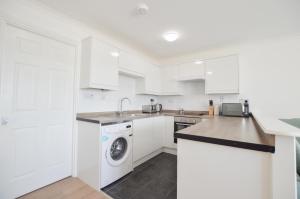 eine Küche mit weißen Schränken und einer Waschmaschine und einem Trockner in der Unterkunft No 8 Westbay Apartment in Oban + 23 Fotos