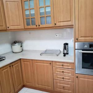 una cocina con armarios de madera y encimeras blancas en Izzahrah 4Rooms Shah Alam, en Shah Alam