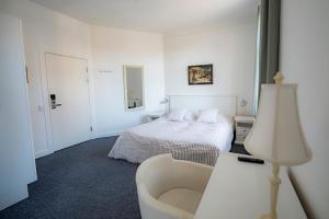 um quarto branco com uma cama e uma cadeira em Det Gamle Posthus em Rønne