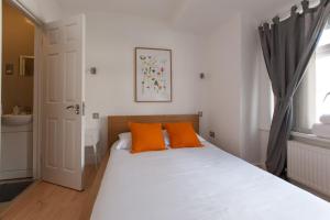 Tooting Rooms by DC London Rooms في لندن: سرير أبيض مع وسائد برتقالية في غرفة النوم