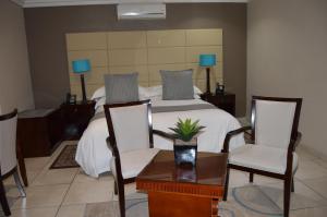 Schlafzimmer mit einem Bett mit 2 Stühlen und einem Tisch in der Unterkunft Lakeview Boutique Hotel & Conference Center in Benoni