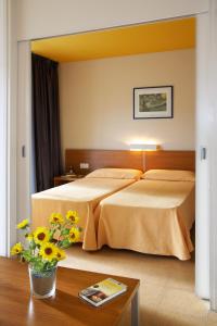 プラヤ・デアロにあるAparthotel Comtat Sant Jordiのベッドと花のテーブルが備わるホテルルームです。