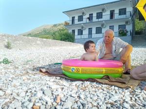 Ein Mann und ein Kind sitzen am Strand mit einem Floß in der Unterkunft B&B BALANI Rooms in Shkodra