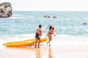 a man and woman walking on the beach next to a yellow kayak at Barceló Huatulco - All Inclusive in Santa Cruz Huatulco