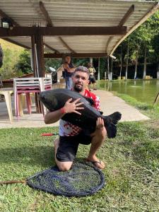 a man sitting on the grass holding a fish at Pesque pague pousada do Carlinho in Pinheiral