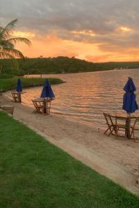 three picnic tables with umbrellas on a beach near the water at Hotel Fazenda Monte Cristo in Piranhas