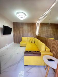 a living room with a yellow couch and a tv at Flat da Babi, MODERNO, LUXUOSO, EQUIPADO e 600mb wifi in Campos do Jordão