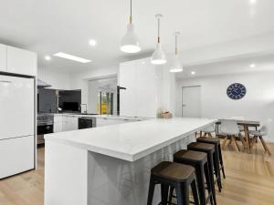 a white kitchen with a large white counter and stools at Puebla Casa 17 in Torquay +13 photos