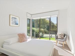 a white bedroom with a bed and a chair at Coast Drive Beach and Golf 31 in Torquay +7 photos