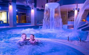 twee personen in een zwembad met een waterval bij Spa Hotel Härmä - Härmän Kylpylä in Ylihärmä