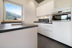 a kitchen with white cabinets and a large window at Sommersbergerhof 2017 in Bressanone
