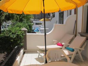 ein gelber Regenschirm auf einem Balkon mit Stühlen und Tischen in der Unterkunft Puerto De Mogan Harbour 371 by El Sirocco in Puerto de Mogán