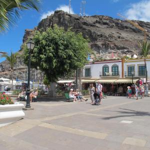 a group of people sitting in a plaza in front of a mountain at Puerto De Mogan Harbour 371 in Puerto de Mogán