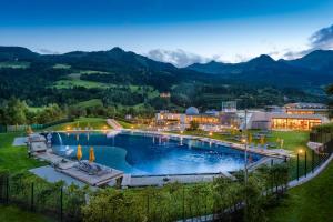 a resort with a large pool with mountains in the background at Hotel Das Gastein - ganzjährig inklusive Alpentherme Gastein & Sommersaison inklusive Gasteiner Bergbahnen in Bad Hofgastein