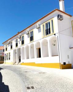 a white building with yellow and white columns at The Bulldog Inn - Duna Parque Group in Vila Nova de Milfontes