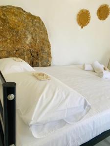 a bed with white sheets and a large rock at Litharaki Guest House in Ano Syros