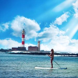 a woman on a paddle board in the water with a lighthouse at Olas de Lobos in Corralejo