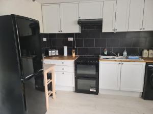 a kitchen with white cabinets and a black refrigerator at Large Brick Chalet sleeps 6 mins to beach and amusements in Leysdown-on-Sea