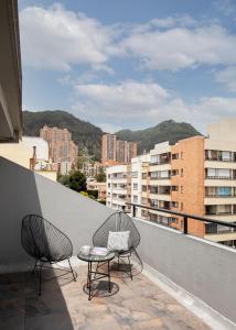 2 Stühle und ein Tisch auf einem Balkon mit Gebäuden in der Unterkunft BOGO - 64 in Bogotá