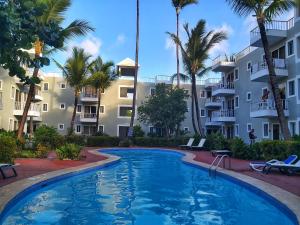 a pool in front of a building with palm trees at Punta Cana Blue Beach Estudio in Punta Cana
