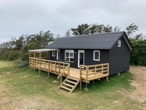 une petite maison noire avec une grande terrasse en bois dans l'établissement Gl. Klitgaard Camping & Cottages, à Løkken