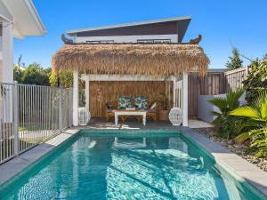 a swimming pool in a backyard with a thatch roof at Kia Orana Island Home with Pool in Casuarina