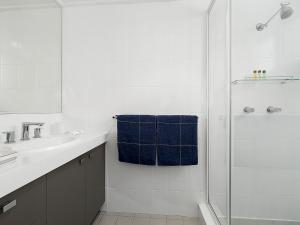 a white bathroom with a shower and a blue towel at Shoreline 6 with Ocean Views To See The Whales in Hastings Point