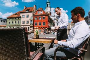 two men sitting at a table with a bottle of wine at STARY RYNEK Old Market Square PREMIUM Apartments & Restaurant Ratuszova AD 1954 room service & mini bar in Poznań