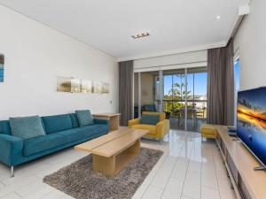 a living room with a blue couch and a tv at Coast Culture 1208 Apartment with complex Pool & Spa in Kingscliff