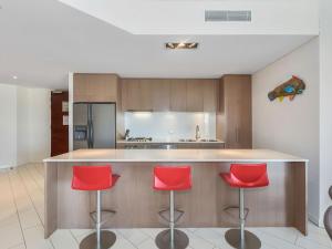 a kitchen with red chairs at a counter at Coast Culture 1208 Apartment with complex Pool & Spa in Kingscliff