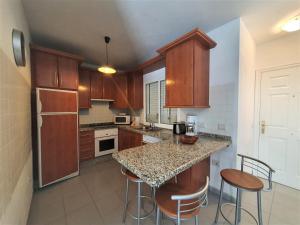 kuchnia z drewnianymi szafkami oraz wyspa z barowymi stołkami w obiekcie Cristi Puerto Santiago Apartment by HRTenerife Net w mieście Puerto de Santiago