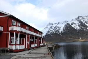 a red building next to a body of water with mountains at Sildpollnes Sjøcamp in Vestpollen