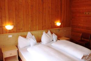 una camera da letto con letto, lenzuola e cuscini bianchi di Albergo Alisander a Corvara in Badia