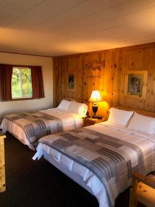 two beds in a room with wooden walls at Holiday Motel in Manistique