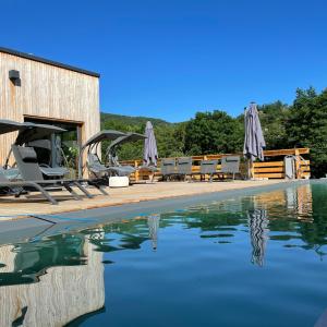 una piscina con sillas y sombrillas junto al agua en Le Volcan des Sens, chambres d'hotes de luxe et SPA, en Torsiac