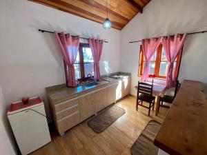 a kitchen with pink curtains and a sink and a table at Chalé vale das Araucárias in Monte Verde