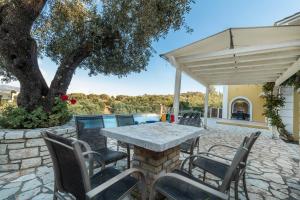un patio con mesa, sillas y un árbol en Agios Stefanos Bay - Villa Dimitris en Ágios Stéfanos